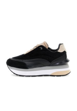 Zwarte en beige sneaker met een dikke witte, grijze en beige zool, bovenwerk van suede en leer, en beige veters, zijaanzicht op een witte achtergrond.