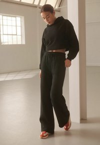 Sort cropped hoodie med lange ærmer, parret med sorte højtaljede sweatpants. Har en løs pasform og snørelukning i taljen. Røde og hvide sneakers.