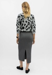 Pull gris avec un imprimé animal noir, associé à une jupe crayon grise à fente arrière. Des chaussures noires complètent la tenue.