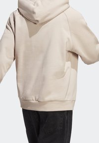 Beige huppari, jossa on rento istuvuus, pehmeä rakenne ja ribattu helma, yhdistettynä tummiin farkkuihin, joissa on takataskut.