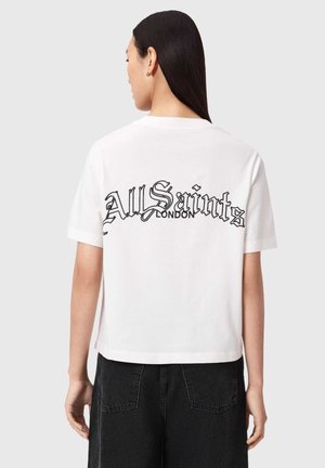 Persoon met lang donker haar draagt een wit cropped T-shirt met de tekst "AllSaints London" op de rug en zwarte high-waist jeans.