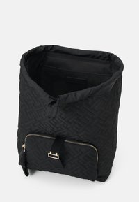 Sac à dos en tissu matelassé noir avec un design à rabat, une poche zippée à l'avant et des accents en métal doré. Doublure intérieure lisse.