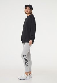 Felpa nera con maniche lunghe, leggings grigi con stampa "LOS ANGELES" e scarpe da ginnastica bianche; outfit casual sportivo.