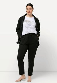 Giacca nera con zip sopra una maglietta bianca con la scritta "IMAGINE" in argento e nero. Completata da pantaloni neri a gamba tapered e sandali argentati.