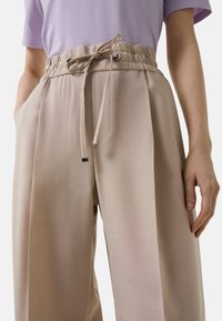 Beige wijdvallende broek met een hoge elastische tailleband, koordsluiting en zijzakken. Glad textiel met een subtiele glans.