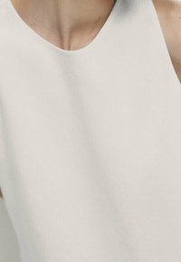 Top senza maniche bianco con una texture liscia, scollatura rotonda e design minimalista, adatto per abbigliamento casual o formale.