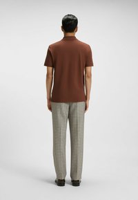 Brun polotröja i slätt tyg, tillsammans med ljusgrå rutiga byxor. Klädseln har korta ärmar och en klassisk krage.