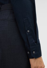 Marineblauwe langesleeve shirt met knopenmanchetten, met een gladde stof en een op maat gemaakte uitstraling. Draagt met gestructureerde donkere broeken.