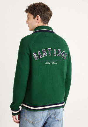 Grön stickad tröja med krage, med vita och marinblå randiga detaljer vid fållen och muddar, samt "GANT 1949" broderat på baksidan.
