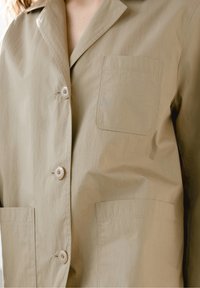 Beige letvægtsjakke med en glat tekstur, knaplukning, en brystlomme og to forreste påsyede lommer.