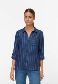 Marineblauwe knoopshirt met verticale witte strepen, voorzien van een borstzak en opgerolde mouwen. Gemaakt van een zachte, gestructureerde stof.