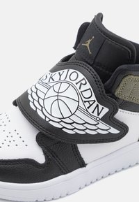 Black and white sneaker featuring a leather upper, strap with "SKYJORDAN" logo, and a rubber sole with perforated toe details.
