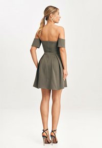 Oliwkowa sukienka typu off-the-shoulder z plisowanym dołem i zapięciem na zamek z tyłu. W połączeniu z czarnymi sandałami na wysokim obcasie. Gładka faktura materiału.