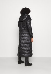 Lång svart pufferjacka med huva, med en glänsande yta, quiltat mönster och ribbade ärmslut, kombinerad med knähöga svarta stövlar.