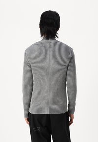 Camisa de manga larga gris de canalé con rayas verticales, con un escote redondeado y una silueta ajustada. El material parece suave y texturizado.