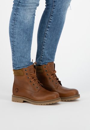 Botas de cuero marrón hasta el tobillo con cuello de ante beige, punta redonda y diseño de cordones. Suela de goma robusta con banda de rodadura para mayor agarre.