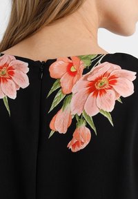 Close-up of a black garment with pink and orange floral print near the back neckline, showing a short zipper and a woman's neck and hair.