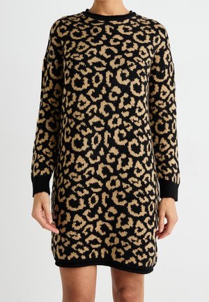 Długa sukienka dzianinowa z nadrukiem w cętki lamparta w kolorze czarno-beżowym, noszona przez osobę widoczną od ramion do połowy ud na jednolitym tle.