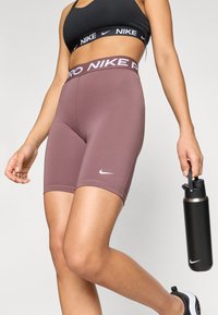 Burgundia Nike Pro lühikesed püksid laia vöökoha ja "Nike Pro" kaubamärgiga, valmistatud siledast ja venivast materjalist; koos musta veepudeli. 