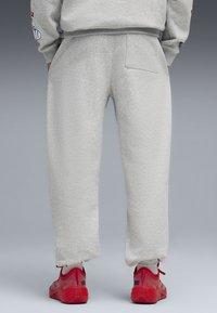 Pantalones de chándal grises con un corte holgado, que cuentan con una cintura elástica, tobillos ajustados y un único bolsillo trasero. Llevados con zapatillas rojas.