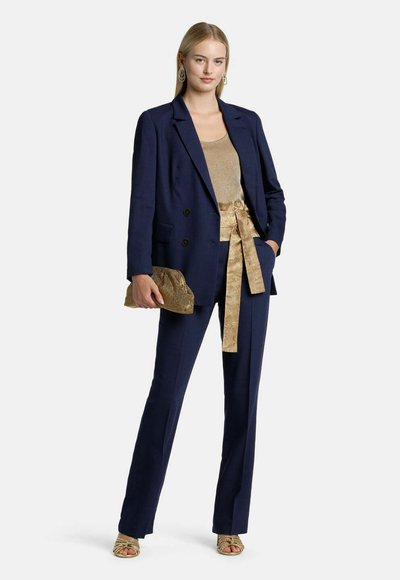 Navy blazer with double-breasted buttons, paired with a gold top and pants featuring a tied belt. Accessories include a gold clutch.