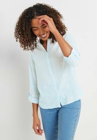 Light blue button-up shirt with daisy embroidery, rolled sleeves, and a relaxed fit. Made from a soft, lightweight fabric.