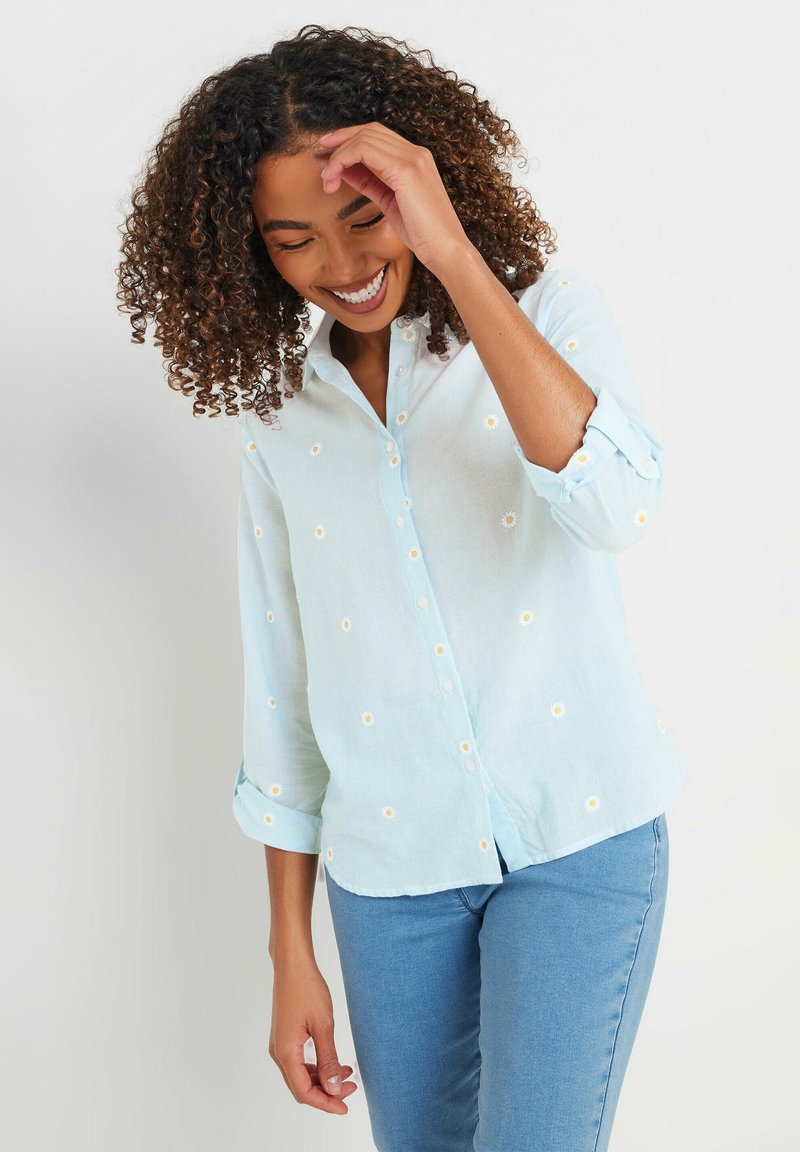 Light blue button-up shirt with daisy embroidery, rolled sleeves, and a relaxed fit. Made from a soft, lightweight fabric.