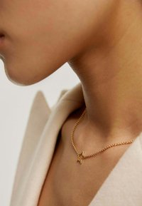 Collar de oro con un colgante en forma de estrella, reposando sobre la piel, con una delicada cadena y textura suave y brillante.