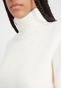 Weißer Rollkragenpullover aus weichem, strukturiertem Stoff mit einem dicken Rippkragen und einem glatten Körperdesign.