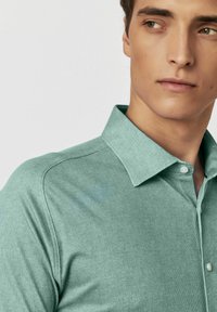 Mintgroene, kortermige blouse met knopen en een subtiel textuurpatroon en een klassieke kraag. Heeft een knoopsluiting en een aansluitend ontwerp.