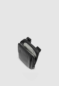 Borsa a tracolla in pelle nera con chiusura a zip, dotata di una singola tracolla e di una morbida fodera interna grigia. Forma rettangolare compatta.