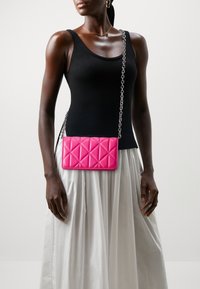 Pink quilted crossbody bag with a silver chain strap, featuring a rectangular shape and smooth texture. The background is neutral.