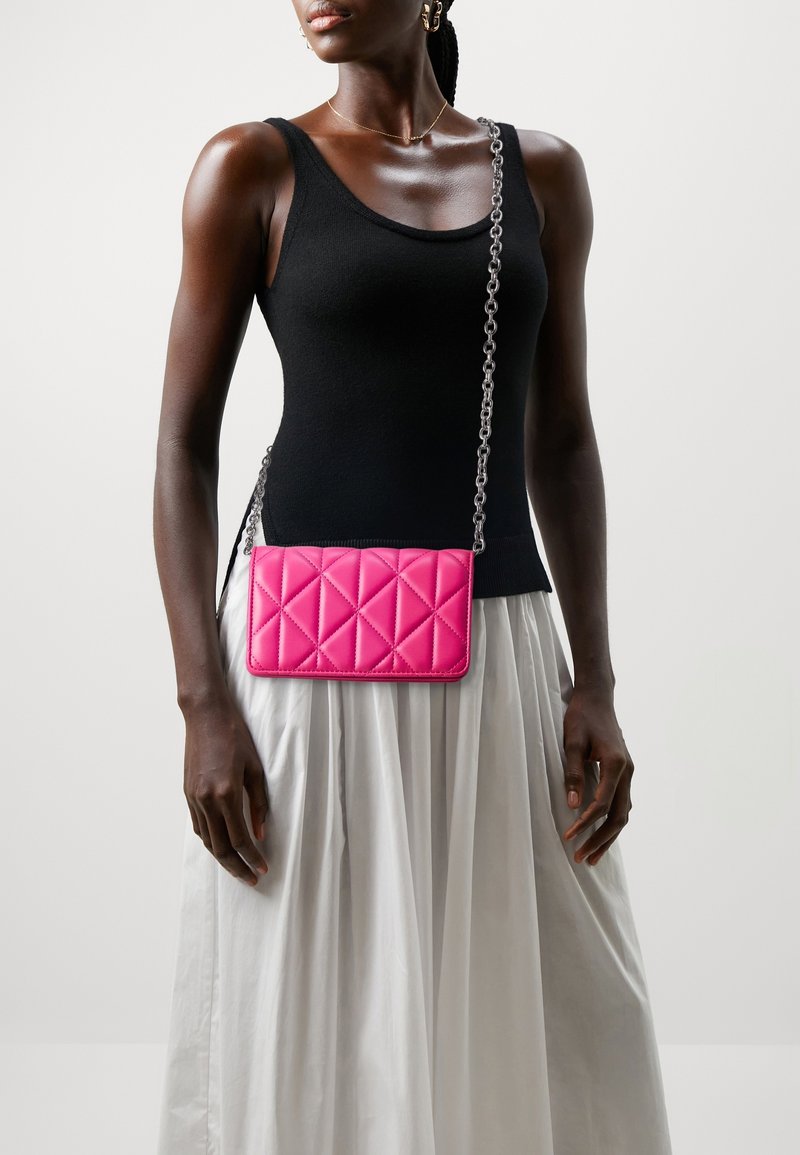 Pink quilted crossbody bag with a silver chain strap, featuring a rectangular shape and smooth texture. The background is neutral.