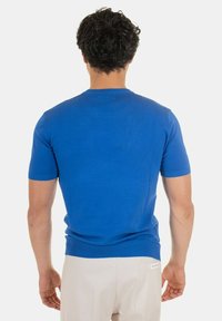 Maglione a maniche corte blu in maglia con design aderente, texture liscia e rifiniture a coste su maniche e vita, visto da dietro.