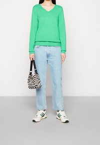 Green v-neck sweater, light blue straight-leg jeans, zebra-print bag, and white sneakers with green accents. Casual outfit with varied textures.