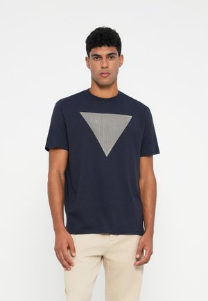 Camiseta azul marino, de mangas cortas, con cuello redondo, que presenta un prominente gráfico triangular a rayas grises en el frente. Material de algodón suave.