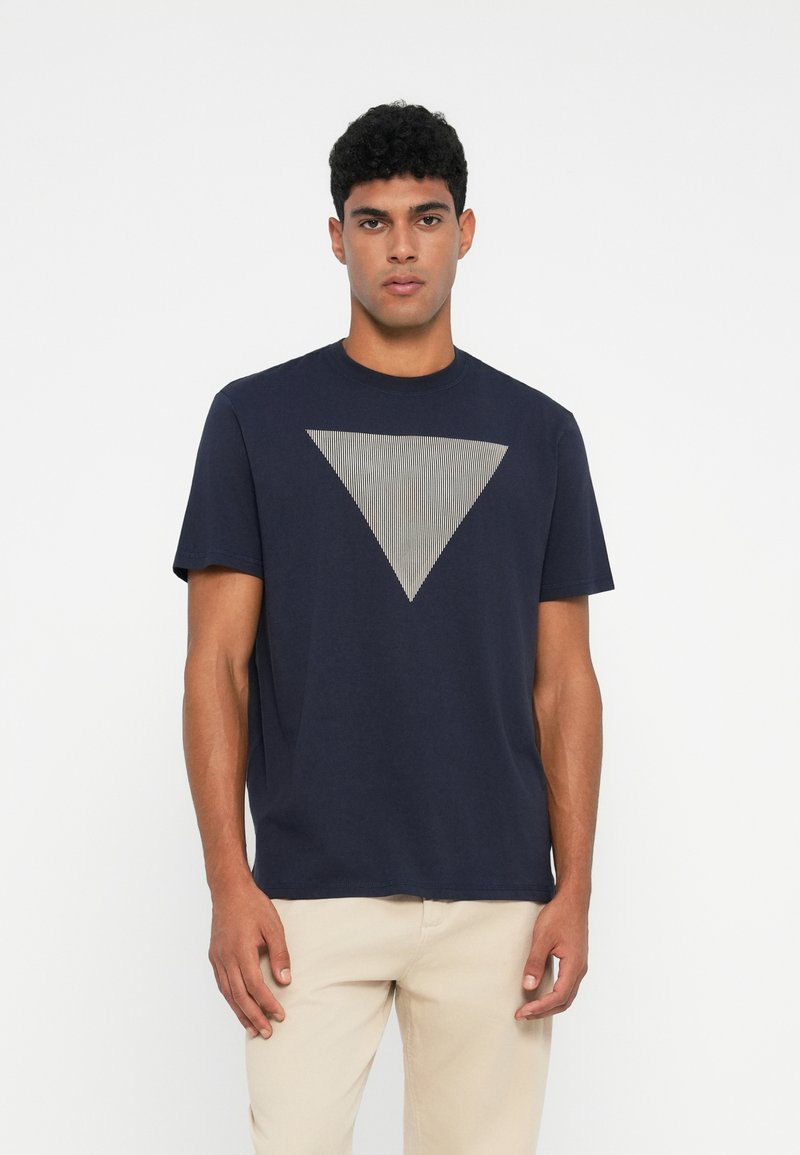 Camiseta azul marino, de mangas cortas, con cuello redondo, que presenta un prominente gráfico triangular a rayas grises en el frente. Material de algodón suave.