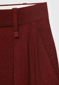 Burgundské kalhoty s vysokým pasem a plochým páskem, zdobené zašitými záhyby a hladkým, měkkým povrchem.