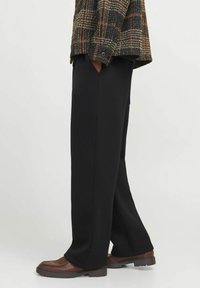 Pantaloni negri cu picioare largi, confecționați dintr-un material moale, având buzunare laterale și un tiv curat. Purtați cu o jachetă în carouri și pantofi maronii.