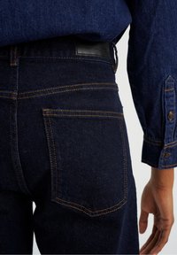 Donkerblauwe denim jeans met oranje stiksels, een leren achterpatch en twee achterzakken met een klassieke pasvorm.