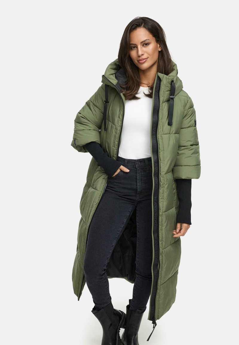 Lång olivgrön puffjacka med huva, som har en framsida med dragkedja, sidofickor och svarta detaljer. Bärs över en vit topp och svarta jeans.