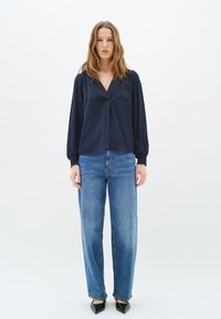 Blusa di raso blu navy con scollatura a V e maniche arricciate, abbinata a jeans chiari a vita alta e décolleté neri a punta.