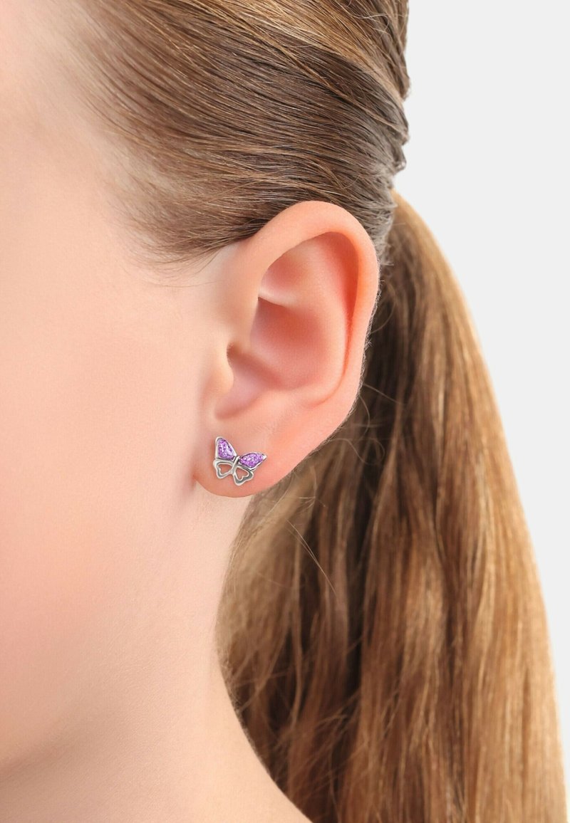 Fjärilshänge med lila accenter, silverram och en delikat design. Positionerad på en models öra mot rakt brunt hår.