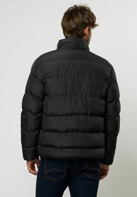 Svart boblejakke med høy krage, quiltede seksjoner og en glatt, blank overflate. Har en avslappet passform og minimalistisk design.