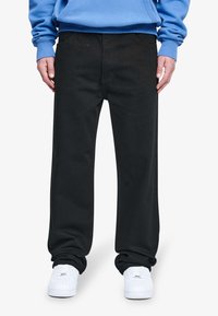 Pantalones negros de pierna recta hechos de algodón, con bolsillos frontales y una textura suave. Llevados con una sudadera azul y zapatillas blancas.