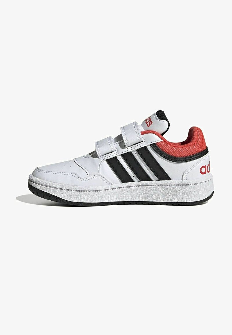 Baskets blanches avec des rayures noires, des accents rouges sur le talon et la languette, des bandes Velcro et une semelle en caoutchouc texturée.