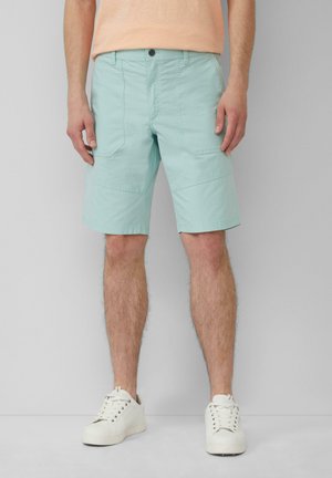 Himmelblaue knielange Shorts aus Baumwolle, mit Vorder- und Hintertaschen, einem Knopfverschluss und einem flachen Bund. Getragen mit weißen Sneakers.