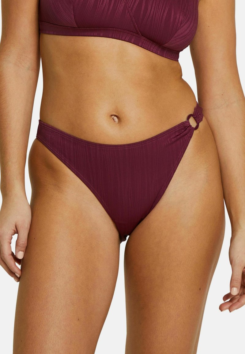Bas de bikini bordeaux avec une texture côtelée, coupe taille haute et un accent en métal circulaire à la taille. Finition en tissu lisse.