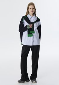 Wit en blauw gestreepte shirt met een losse fit, gecombineerd met zwarte wijde broek en een marineblauwe trui over de schouders.