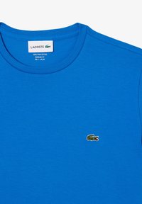 Blå T-shirt lavet af 100% Pima-bomuld, med rund hals og et lille grønt krokodillelogo på venstre bryst. Regular fit design.